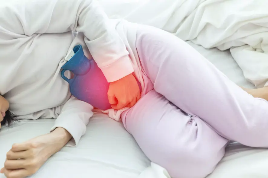 Frau mit Blasenentzündung liegt mit Wärmflasche im Bett