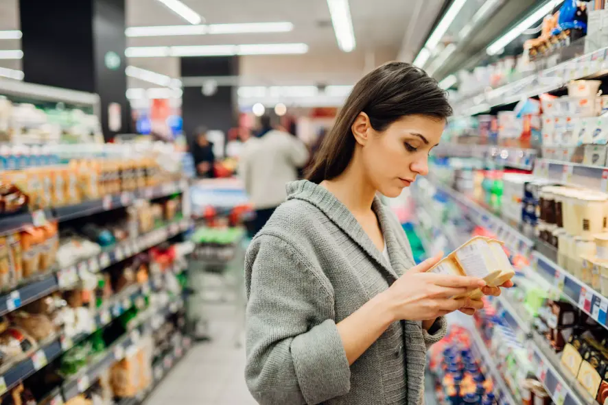 Junge Frau prüft ein Produkt beim Einkaufen im Supermarkt wegen Lebensmittelunverträglichkeit