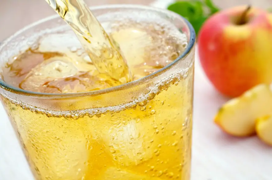 Kühle Apfelschorle wird in ein Glas eingegossen, Fruchtsaftschorlen können bei Mundtrockenheit helfen