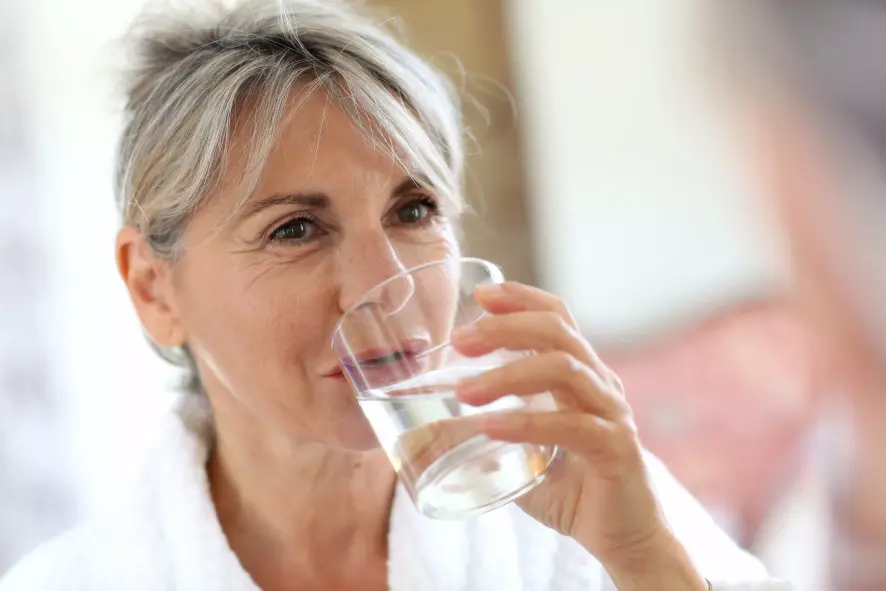 Seniorin trinkt aus einem Wasserglas, ein gutes Mittel gegen Mundtrockenheit